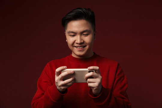 Image of joyful young asian man playing video game on mobile phone