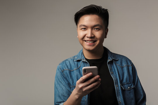 Image of happy handsome asian man smiling and using smartphone