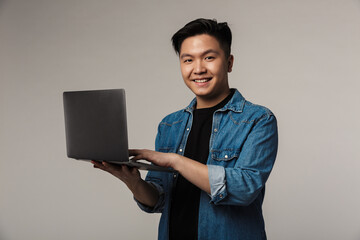 Image of cheerful handsome asian man smiling and using laptop