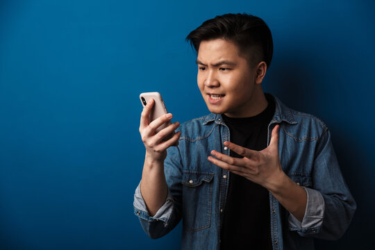 Image of angry handsome asian man making video call on cellphone