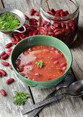 Red kidney bean cooked in tomato sauce garnished with parsley in green bowl on rustic wooden table, closeup, healthy vegan protein food concept