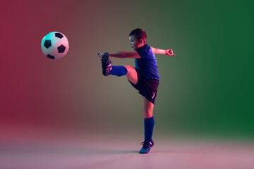 Fototapeta na wymiar Emotions. Teen male football or soccer player on gradient background in neon light. Caucasian boy training, practicing on the run, in jump. Concept of sport, competition, winning, motion, action.