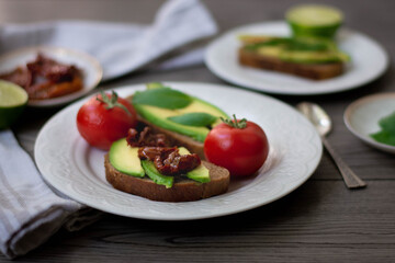 Bruschetta style rye bread toasts with avocado, sun-dried tomatoes, basil, dill and lime. Rustic dark wooden background