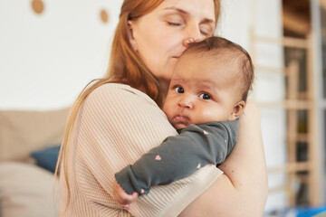 Warm-toned closeup portrait of loving adult mother embracing cute mixed-race baby while enjoying...