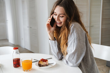 Obraz na płótnie Canvas Photo of woman laughing and talking on cellphone while having breakfast