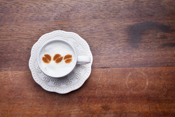 A retro cup with coffee cream. Food art creative concept image, cute drawing with cinnamon powder over milk cream on a wooden background.