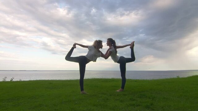 Two women in activewear pposing on the camera and showing yoga Lord of the Dance pose
