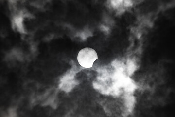 Partial solar eclipse close-up on a background of gloomy clouds.