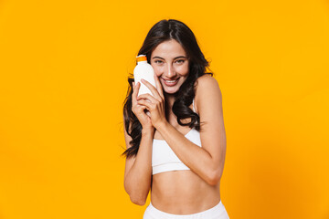 Image of happy woman in swimsuit holding sunscreen and smiling