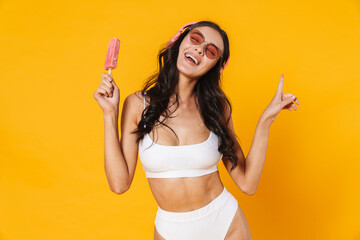 Image of happy woman in headphones eating ice cream while dancing