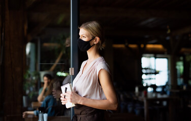 Fototapeta na wymiar Side view of waitress with face mask standing at the door in restaurant.