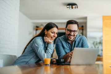 Portrait of a cute smiling couple looking at laptop together at home. - Powered by Adobe