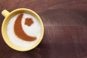 A rustic mug with coffee cream. Food art creative concept image, drawing with cinnamon powder over wooden background.
