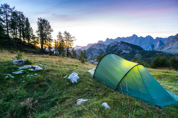 A tent glows under a moon night sky at twilight hour. Julian Alps, Triglav National Park, Slovenia.