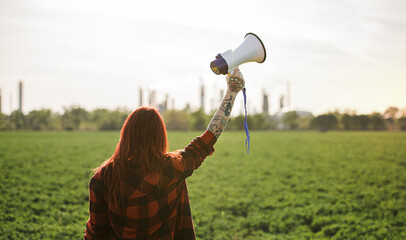 Rear view of woman activist with megaphone outdoors by oil refinery, protesting.