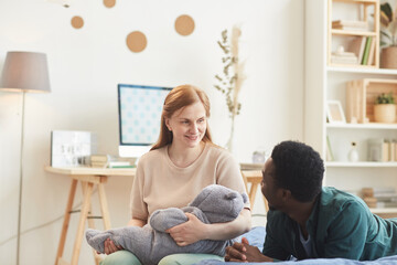 Portrait of happy interracial family with baby boy looking at each other while sitting on bed in...