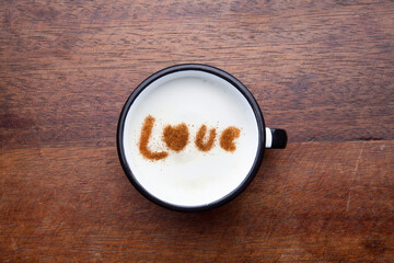 A rustic mug with coffee cream. Food art creative concept image, drawing with cinnamon powder over wooden background.