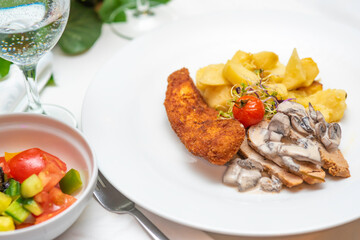 Main meal with breaded meat, mushroom, potato, white sauce, fried tomato and fresh mixed vegetables
