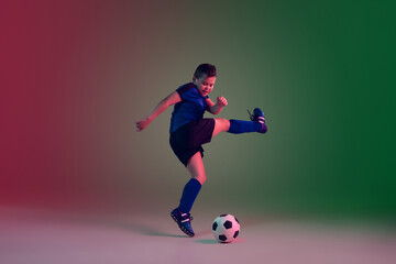 Winner. Teen male football or soccer player on gradient background in neon light. Caucasian boy training, practicing on the run, in jump. Concept of sport, competition, winning, motion, action.