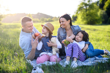 Happy family with two small daughters sitting outdoors in spring nature, having picnic.