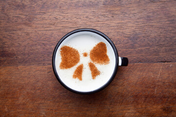 A rustic mug with coffee cream. Food art creative concept image, drawing with cinnamon powder over wooden background.
