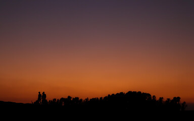 Naklejka na ściany i meble People walking under the orange sky after sunset