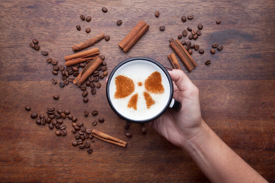A rustic mug with coffee cream. Food art creative concept image, drawing with cinnamon powder over wooden background.

