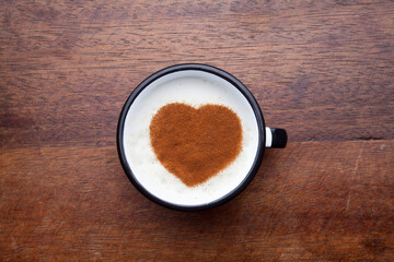 A rustic mug with coffee cream. Food art creative concept image, drawing with cinnamon powder over wooden background.
