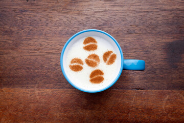 A rustic mug with coffee cream. Food art creative concept image, drawing with cinnamon powder over wooden background.
