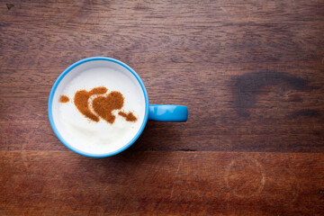 A rustic mug with coffee cream. Food art creative concept image, drawing with cinnamon powder over wooden background.
