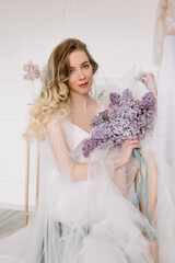 Fototapeta premium Beautiful girl woman bride in a delightful wedding dress with a bouquet of flowers dancing in front of a mirror portrait of a blonde with blue eyes