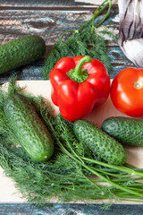 vegetables, Bulgarian peppers, dill, cucumbers on a light cutting Board, dark wooden background
