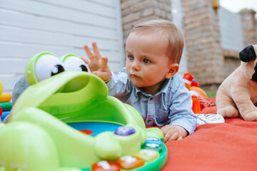 A beautiful caucasian child in the yard is playing with toys on a blanket