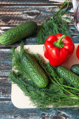vegetables, Bulgarian peppers, dill, cucumbers on a light cutting Board, dark wooden background