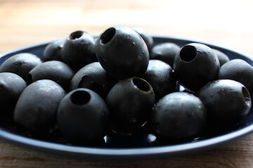 Bowl of black olives. Black canned pitted olives in a dark blue glass bowl on a rustic wooden table. Close-up, selective focus