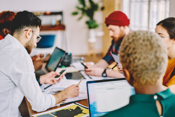 Multicultural group of young people dressed in smart casual wear teamworking on design project having briefing meeting in office.Creative hipster students collaborating on developing business strategy