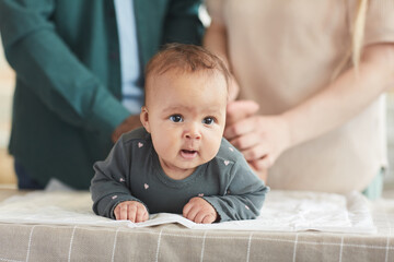 Close up portrait of cute mixed-race baby looking at camera while lying on changing table with...