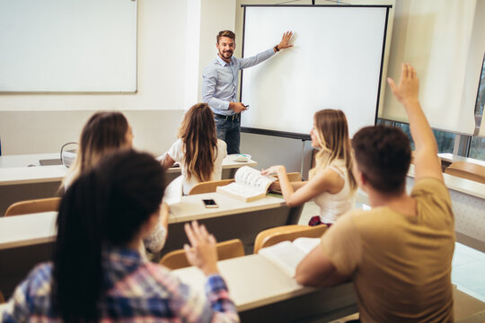 Smiling teacher standing in front of students and showing something on white board in classroom