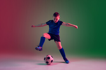 Fototapeta na wymiar Winner. Teen male football or soccer player on gradient background in neon light. Caucasian boy training, practicing on the run, in jump. Concept of sport, competition, winning, motion, action.