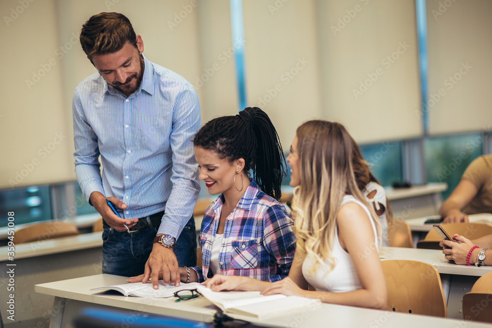 Wall mural  Group of smiling students and teacher with notebook in classroom