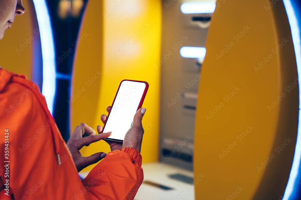 Poster back view of female person using mobile phone banking app while standing front atm cashpoint machine