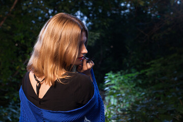 beautiful blonde woman in a black dress and a blue shawl in forest