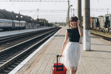 Female brunette traveler with red suitcase walking on raiway station