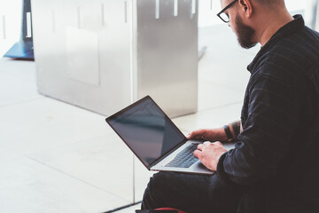 Cropped view of bearded male freelancer installing app for remote work at modern laptop device with mock up area sitting in modern office.Young man web designer updating software on netbook