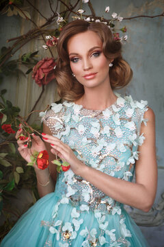 Beautiful girl in an airy turquoise dress on the terrace near a blooming rose bush.