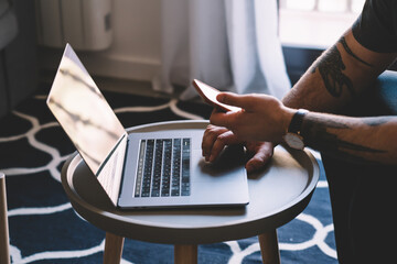 Cropped view of hipster guy searching information on modern laptop computer on website and sharing...
