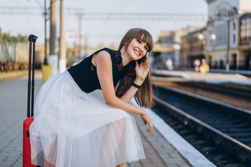 Female traveler with red suitcase waiting train on railway station