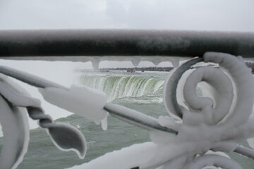 Stunning, breathtaking, powerful Niagara Falls in winter, view from Ontario through an cold frozen fence encased in ice