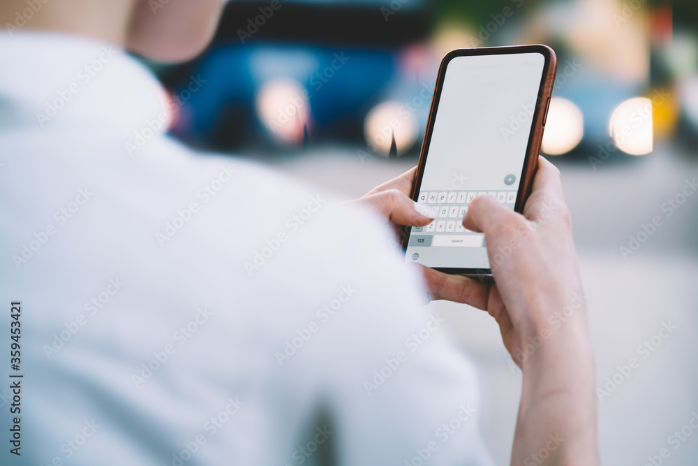 Aufkleber cropped back view of young woman holding smartphone in hands and typing text on keyboard of modern d