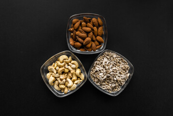 Almond, cashew and sunflower seeds in a small plates which standing on a black table. Nuts is a healthy vegetarian protein and nutritious food.
